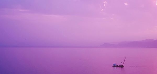 Fishing boat sailing on sea against sky during sunset