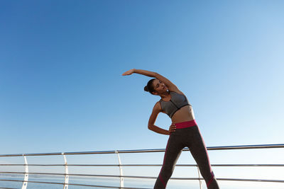 Woman exercising while standing against sea and sky