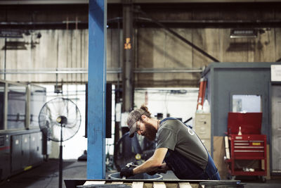 Side view of blue collar worker using hammer and chisel in steel factory