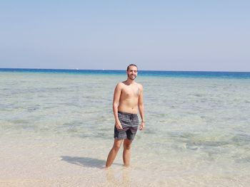 Portrait of shirtless man standing in sea against clear sky