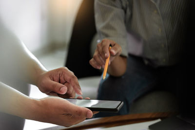 Midsection of people having discussion while holding smart phone and pencil