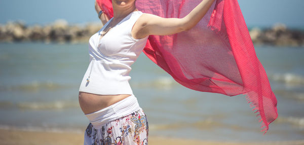 Midsection of pregnant woman with scarf standing at beach