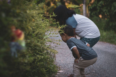 Side view of siblings bending on road by plants