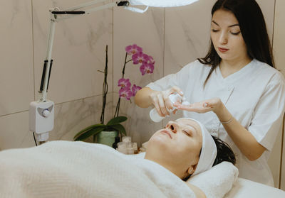 A girl cosmetologist squeezes foam for the face of a patient on a massage table.