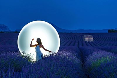 Rear view of woman standing by purple flower on field against sky