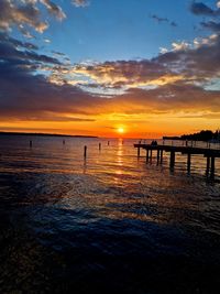 Silhouette wooden posts on beach against sky during sunset