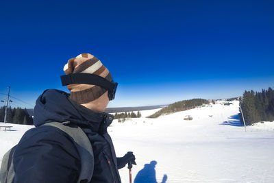 Man standing on snow covered mountain against blue sky