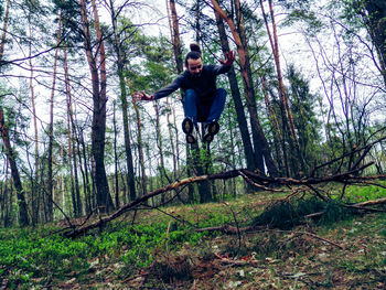 Young man jumping over broken branches against trees in forest