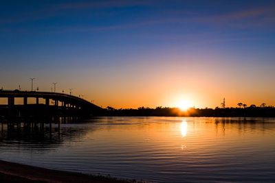 Silhouette bridge over river against sky during sunset