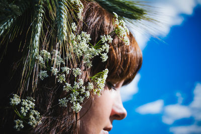 Close-up of flowers on woman head against blue sky during sunny day