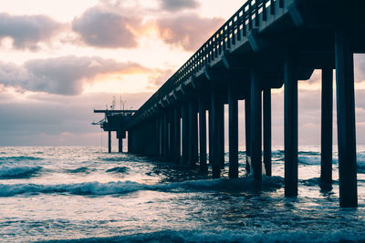 Pier on sea against cloudy sky during sunset