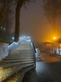 Footpath by illuminated trees against sky during sunset