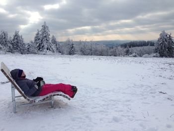 Side view of woman relaxing on lounge chair over snow covered field