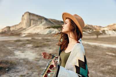 Side view of woman wearing hat standing against mountain