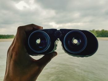 Cropped hand holding binoculars against lake