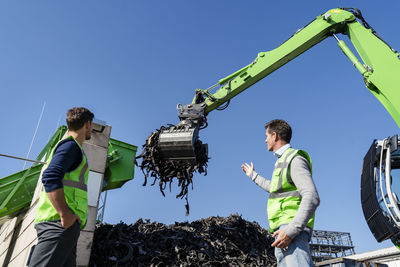 Mature man discussing over excavator with colleague at recycling center