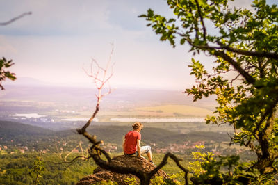 Man sitting on cliff against sky