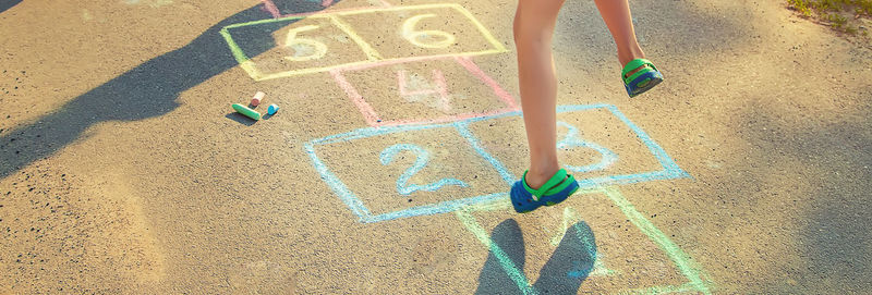 Low section of girl playing hopscotch on road