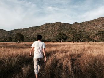 Rear view of man walking on grassy field against mountains