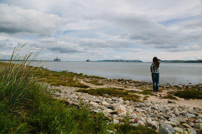 Rear view of woman standing on beach against sky