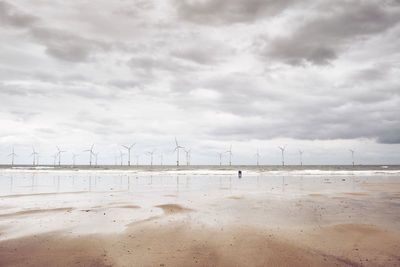 A couple look out to sea towards a wind turbine farm.