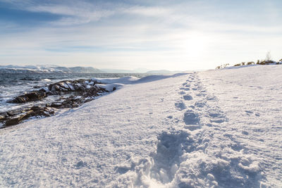 Footprints in snow by sea against sky