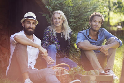 Portrait of smiling friends sitting with vegetable crate on grassy field