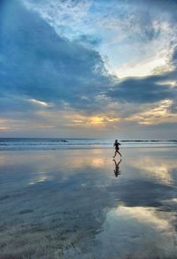 Woman running on beach against sky during sunset