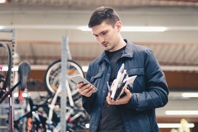 A young man with a phone and goods in his hands stands in the store.