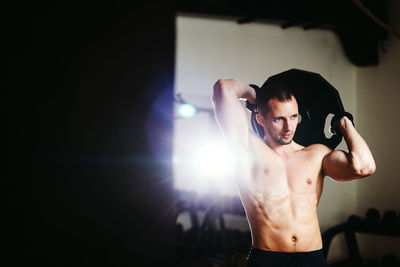 Shirtless muscular man lifting weights while standing in gym