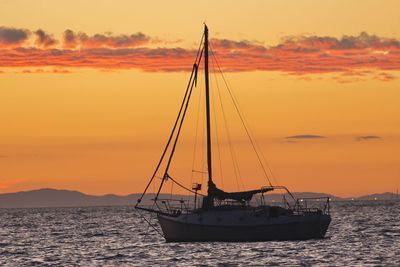 Silhouette sailboat on sea against romantic sky at sunset