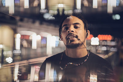 Portrait of young man biting necklace seen through glass at night