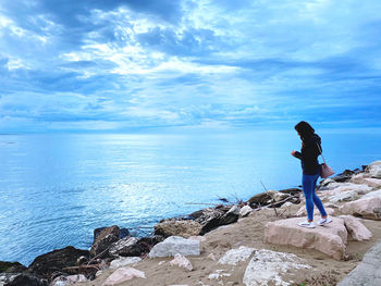 Woman standing on rock by sea against sky