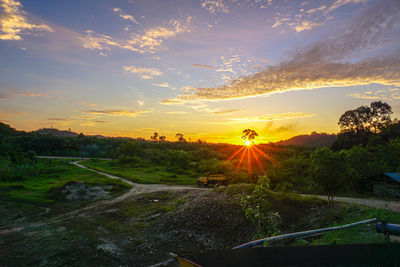 Sunlight streaming on landscape against sky during sunset