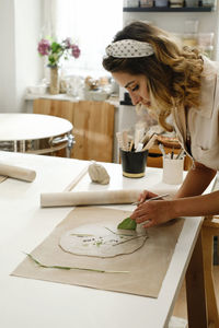 Woman decorating with flowers rolled clay, making ceramic plate in studio with floral pattern