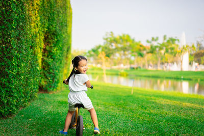 Full length portrait of girl smiling while cycling on grass by trees