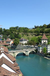 Bridge over river amidst buildings against clear blue sky