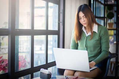 Mid adult woman using mobile phone while sitting on table