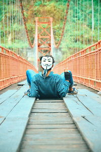 Man wearing mask while lying on footbridge