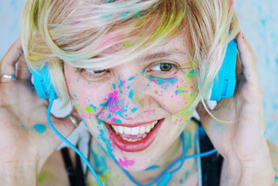 Close-up of happy woman covered in powder paint wearing headphones