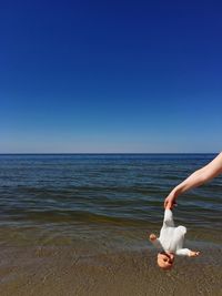 Cropped hand of woman holding doll at beach against clear sky