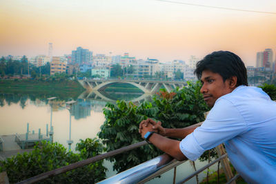 Side view of man leaning on railing against river in city