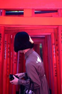Side view of young woman standing against red torii