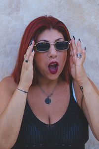 Portrait of young woman wearing sunglasses against wall