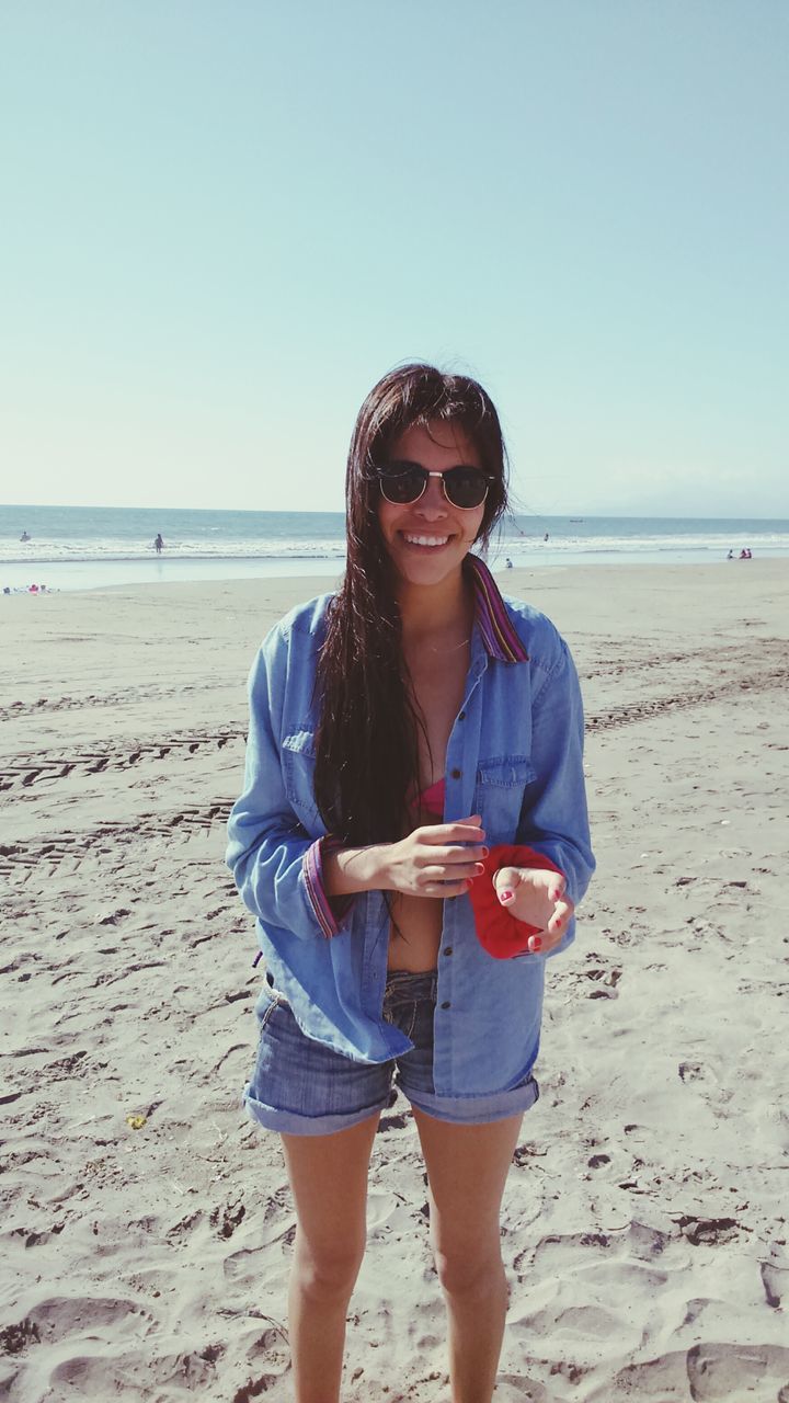 beach, sea, clear sky, sand, young adult, shore, lifestyles, horizon over water, leisure activity, person, casual clothing, young women, looking at camera, water, standing, copy space, portrait, front view