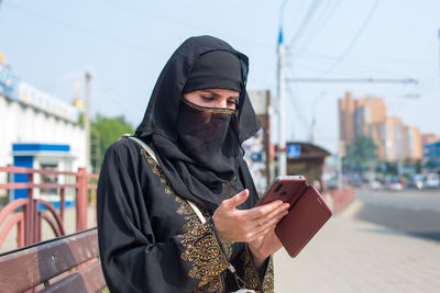 A muslim woman in black national clothes on the street carefully reads a message on her phone.