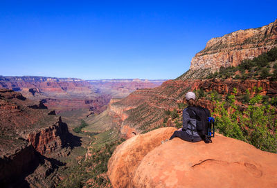 Woman sitting on rock against clear blue sky