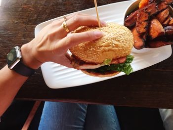 Cropped hand of woman holding burger at table