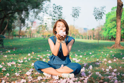 Woman blowing flowers while sitting on field at park