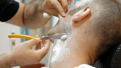 Barber doing shaving of mature man in salon